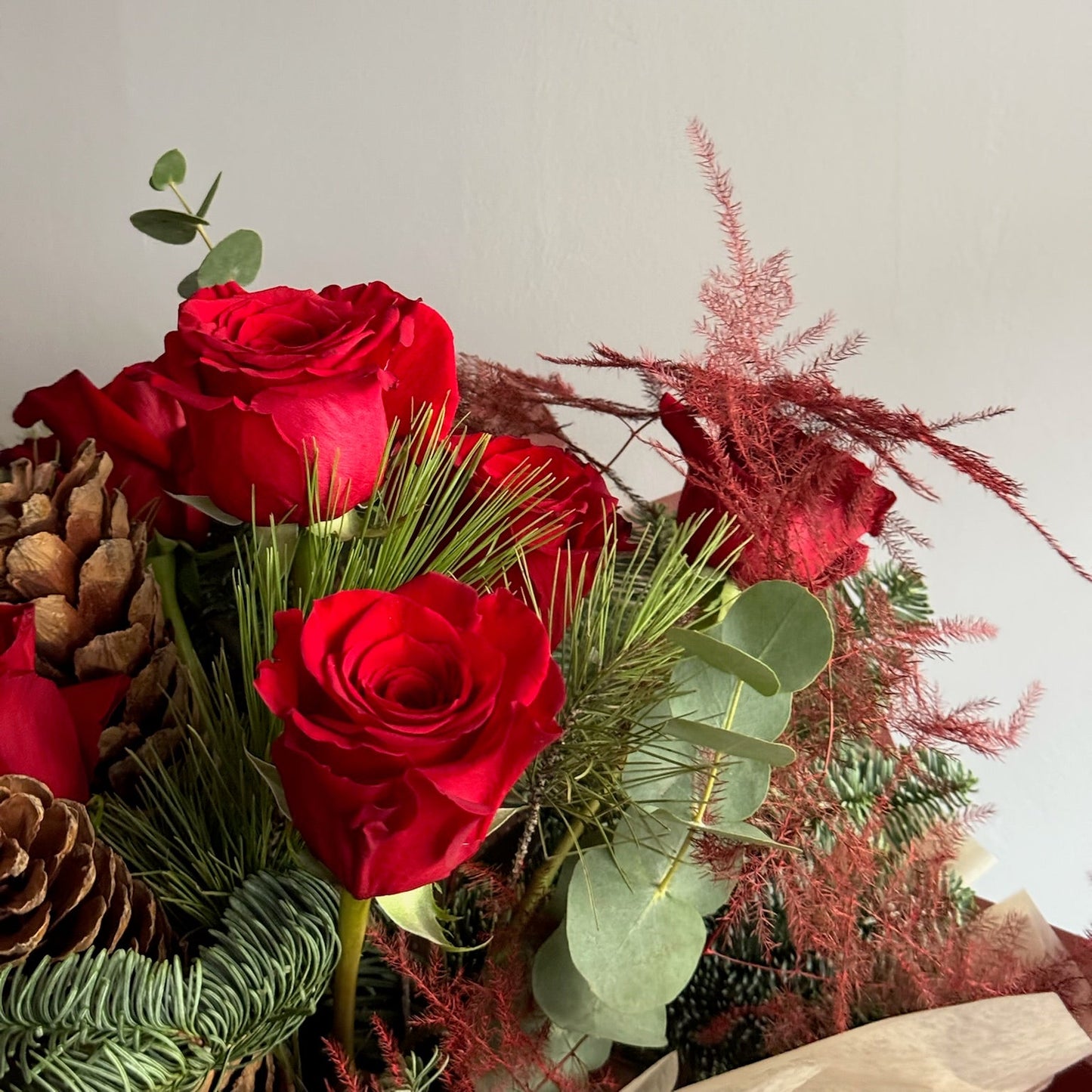 Bouquet of red roses with greenery and decorative elements on a light background