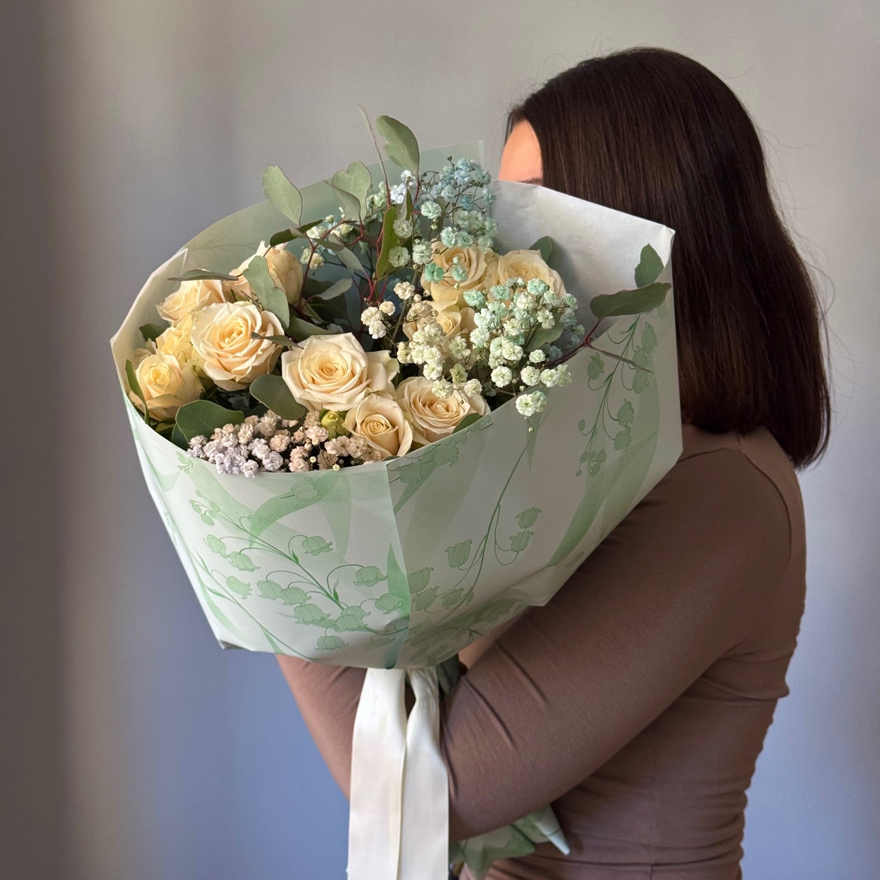 Person holding a bouquet of flowers wrapped in green paper with a white background