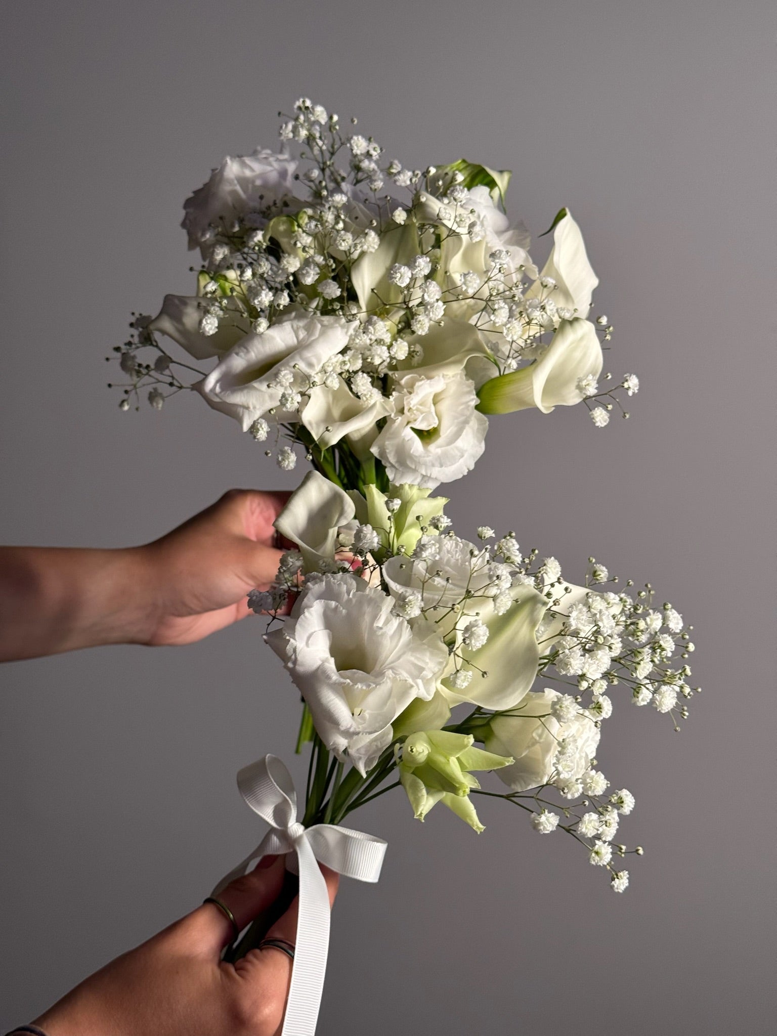 Bouquet of white flowers held by a hand against a gray background