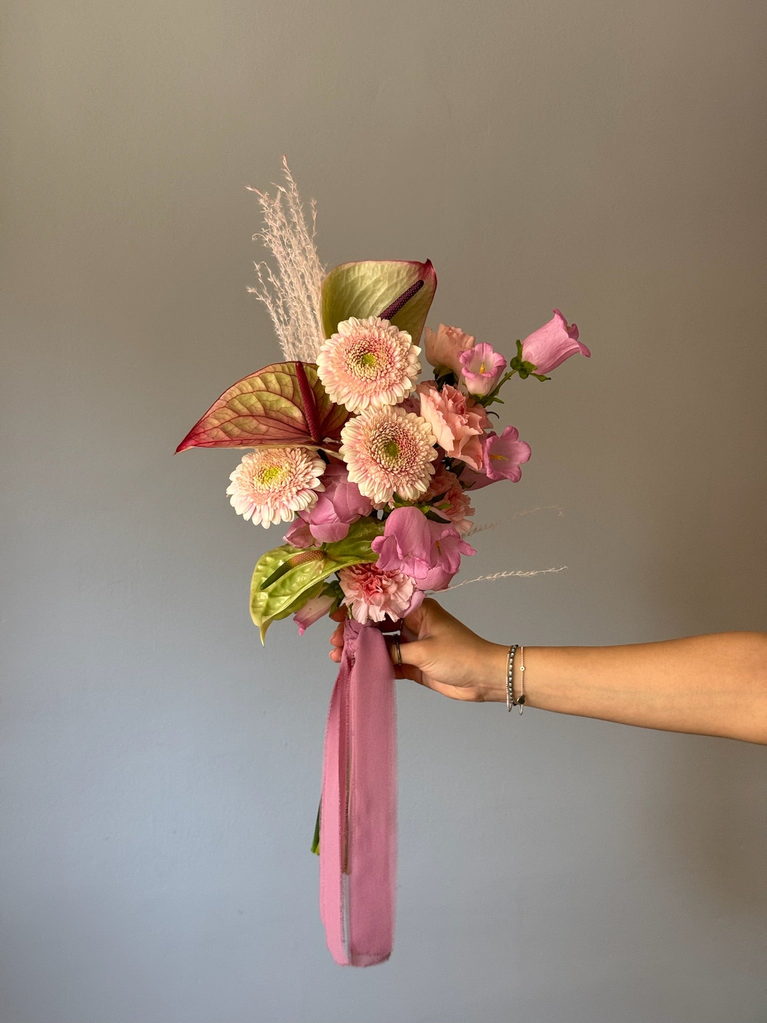 Pink and green flowers in a bouquet held by grey background 