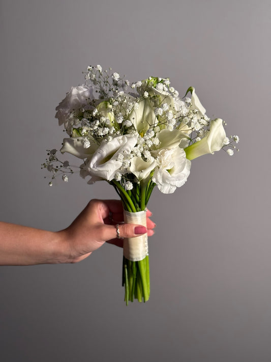 Hand holding a bouquet of white flowers against a gray background
