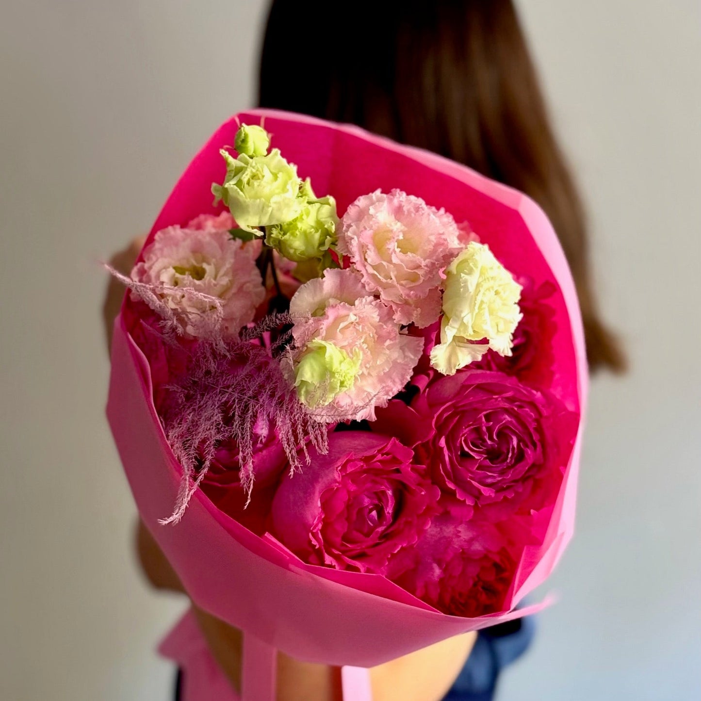 Bouquet of pink and green flowers wrapped in pink paper held by a person.