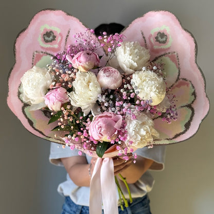 Butterfly bouquet wrapping paper with white and pink peonies held on grey background 