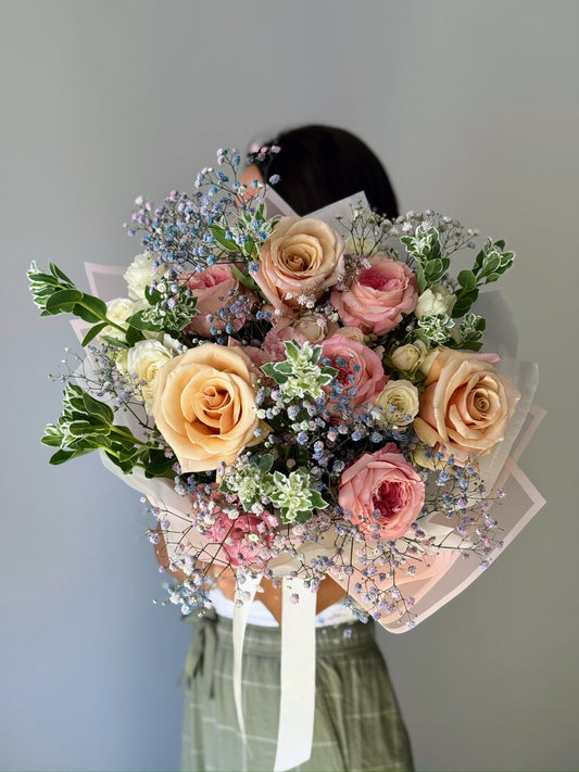 Buchet de flori ținut în mână pe fundal gri roses and more