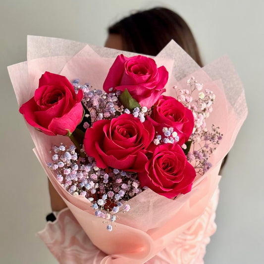 Bouquet of red roses with pink paper wrap held by a person against a neutral background