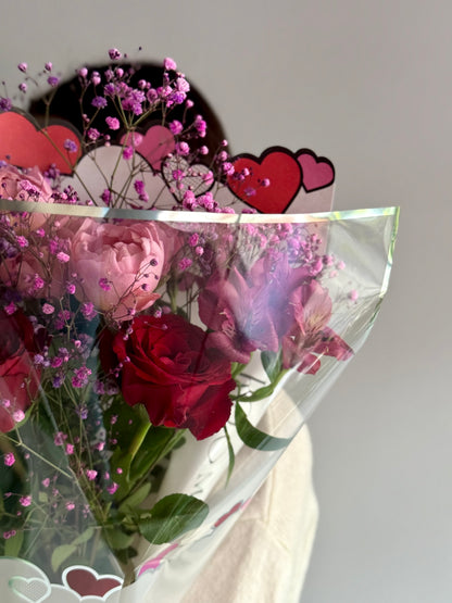 Bouquet of red roses and pink flowers with heart-shaped decorations on a gray background