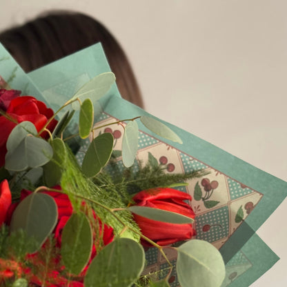 Bouquet of red roses and greenery on a decorative card with a patterned border.