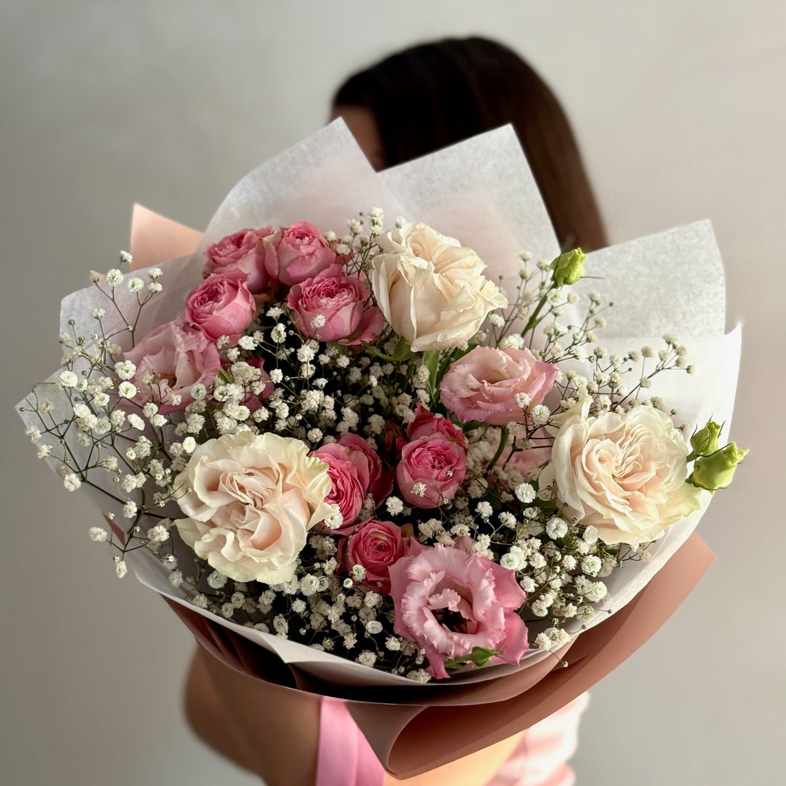 Bouquet of pink and white roses held by a person against a neutral background