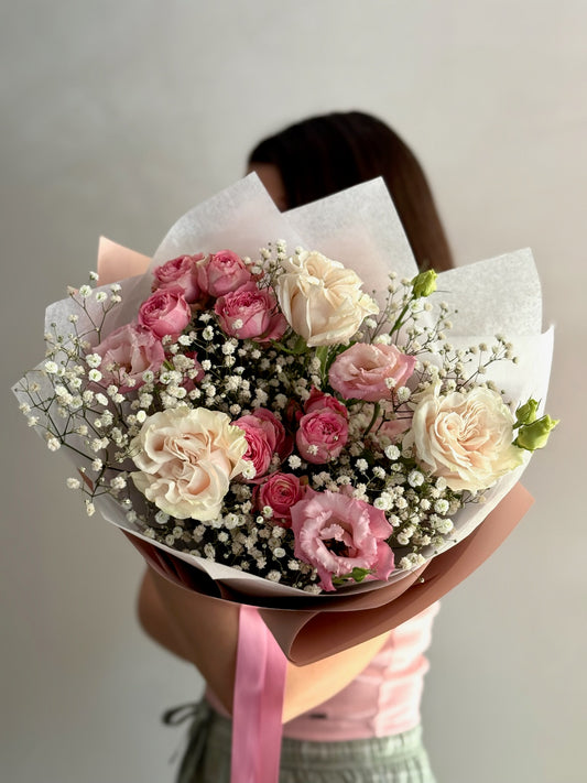 Bouquet of pink and white roses held by a person against a neutral background