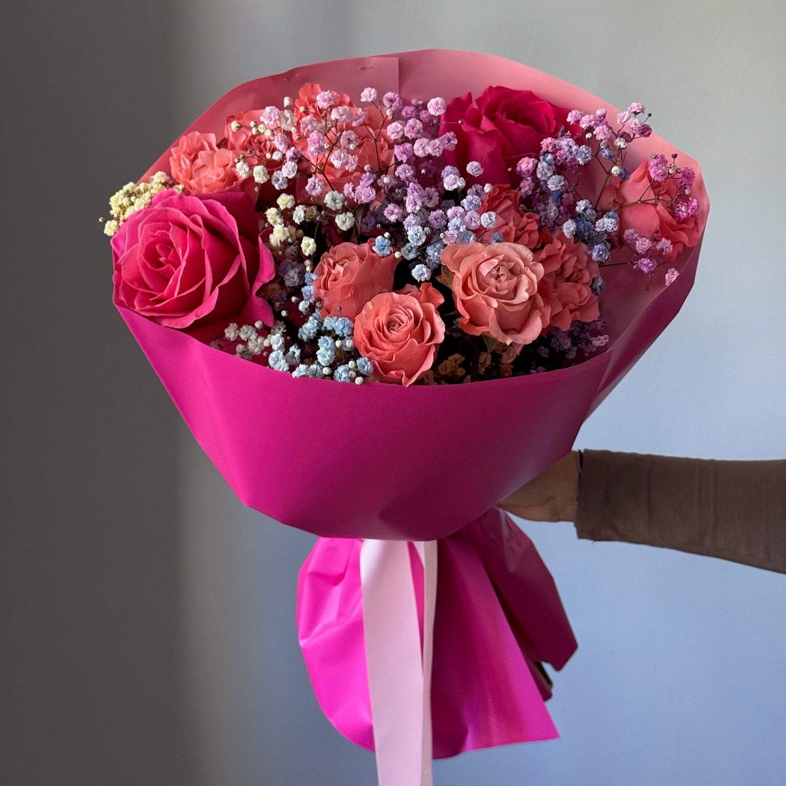 Bouquet of flowers wrapped in pink paper held by a person against a neutral background