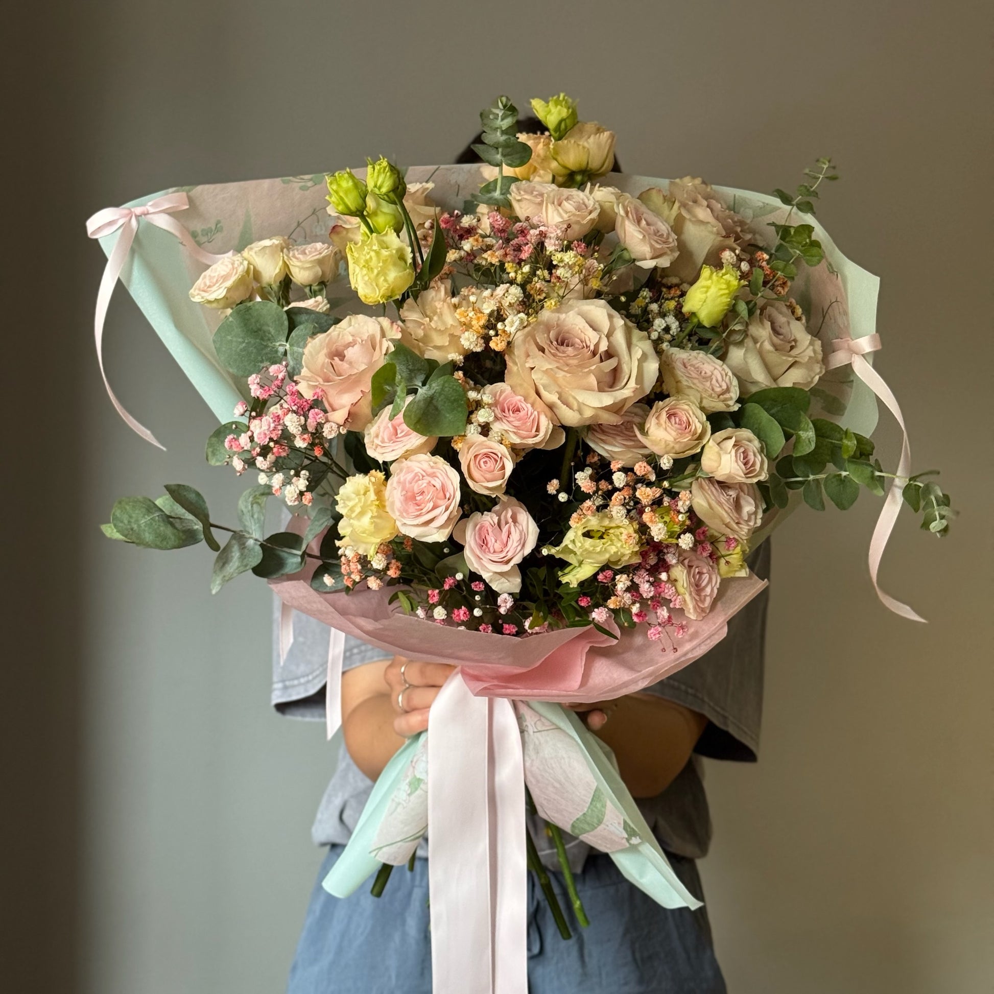 Pink flowers wrapped in a bouquet with bows hel by person on grey background 
