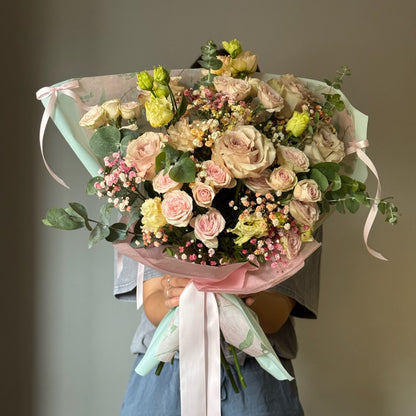 Pink flowers wrapped in a bouquet with bows hel by person on grey background 
