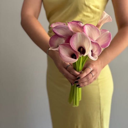 Person holding a bouquet of pink and white flowers wearing a yellow dress against a plain background