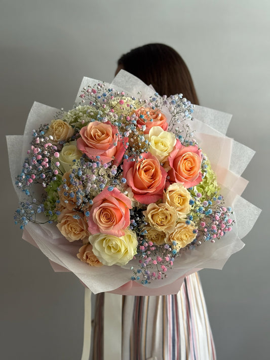 Bouquet of pastel-colored roses with decorative elements held by a person against a neutral background