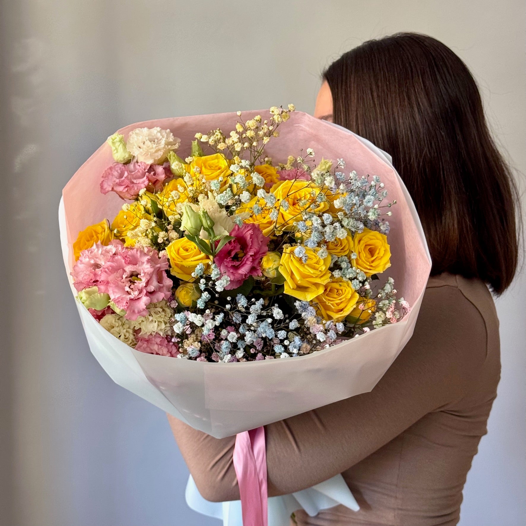 Person holding a large bouquet of colorful flowers against a neutral background