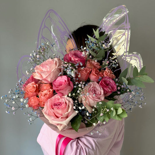Person wearing a butterfly costume holding a bouquet of pink and orange roses.