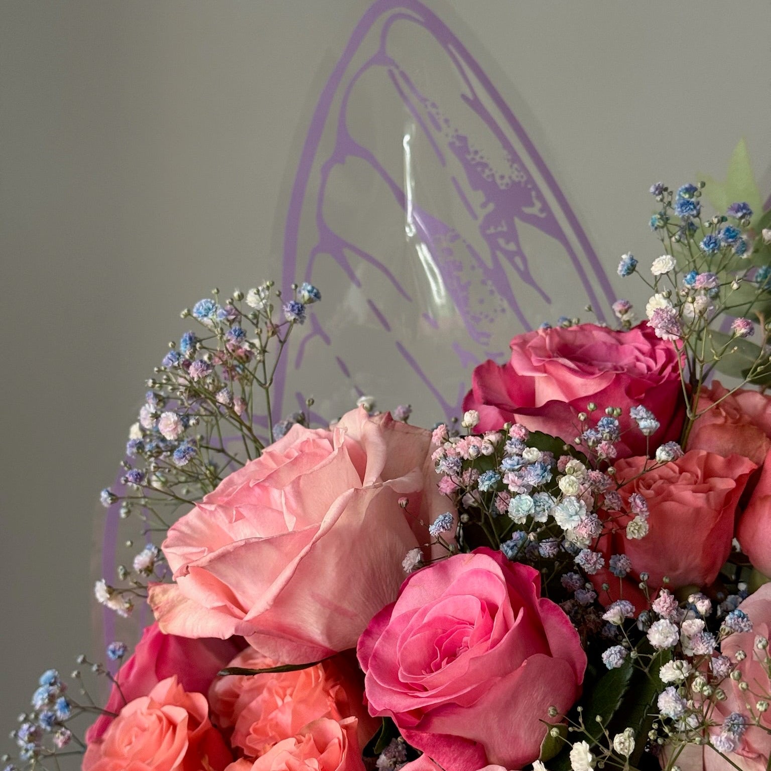 Bouquet of pink roses with small white and blue flowers against a neutral background