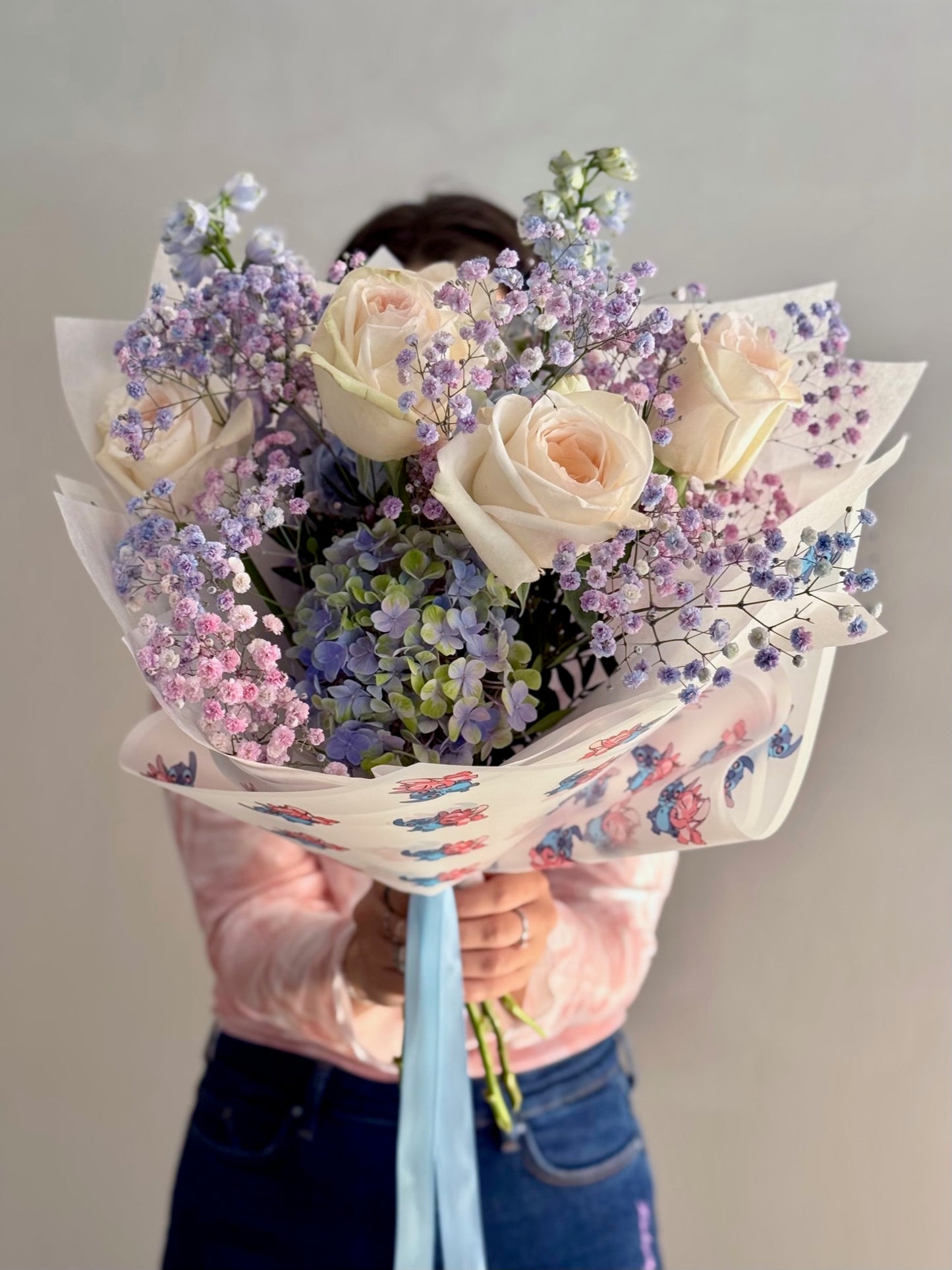 Person holding a bouquet of flowers wrapped in colorful paper against a plain background
