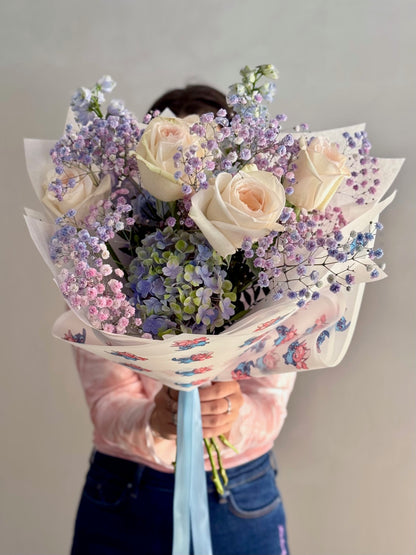 Person holding a bouquet of flowers wrapped in colorful paper against a plain background