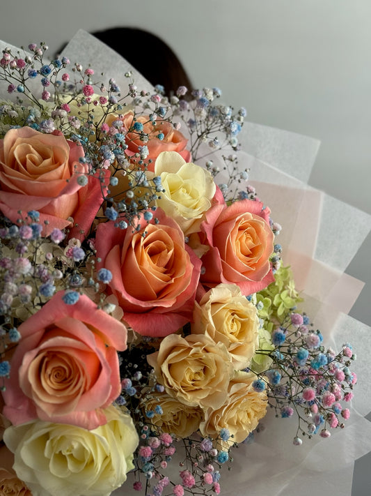 Bouquet of pink, yellow, and orange roses with small flowers on a light background