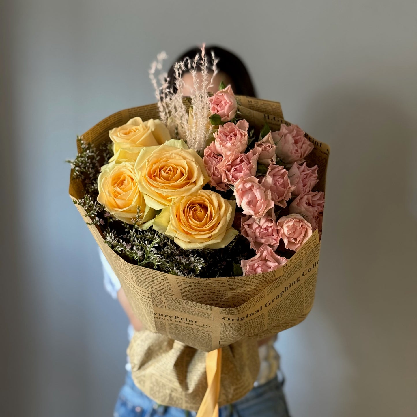 Yellow and pink flowers wrapped in vintage newspaper wrapping paper held on grey background 