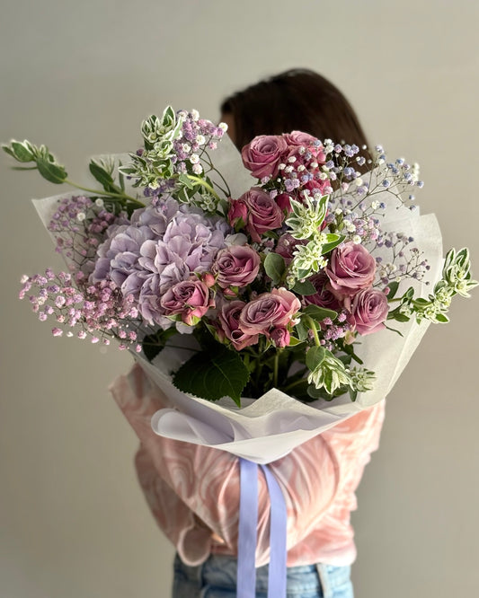 Person holding a bouquet of purple and pink flowers against a plain background