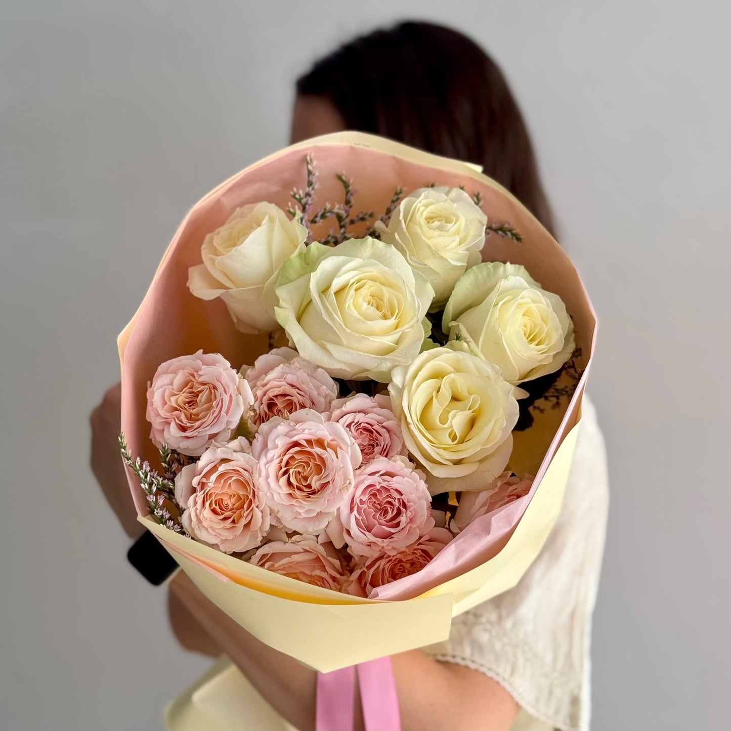 Bouquet of pink and white roses held by a person against a plain background