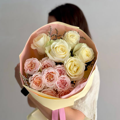 Bouquet of pink and white roses held by a person against a plain background