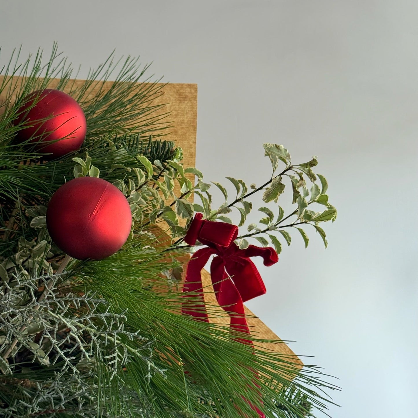 Decorative arrangement with red ornaments and a bow on a wooden board against a light background