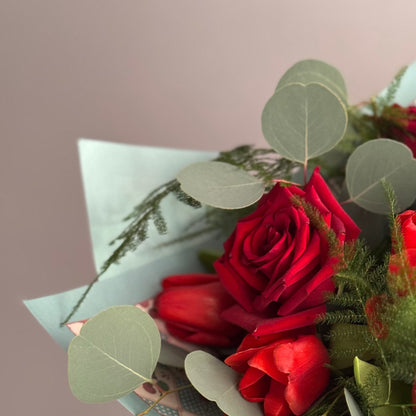 Bouquet of red roses with greenery in a light blue paper wrap on a neutral background