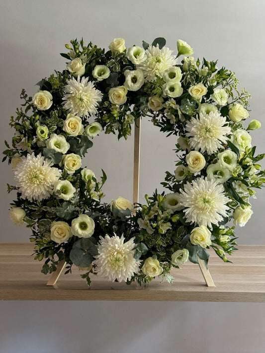 Floral wreath with white and green flowers on a wooden stand against a gray background