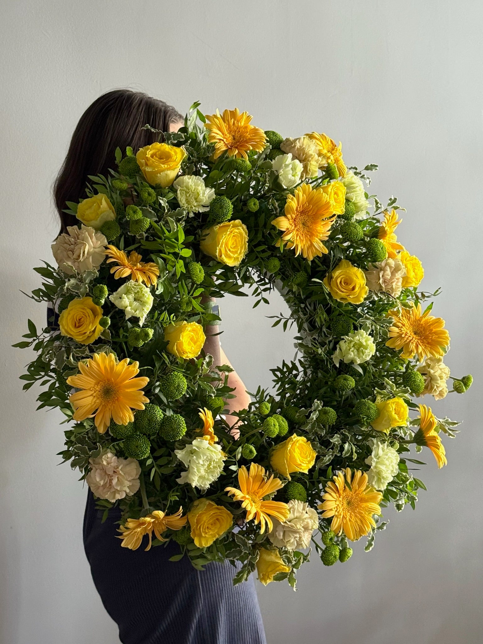 Person holding a floral wreath with yellow and white flowers against a plain background