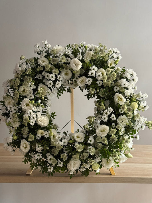 Floral wreath with white and green flowers on a wooden stand against a gray background