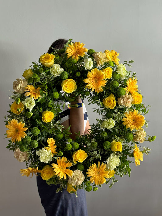 Floral wreath with yellow and green flowers on a plain background