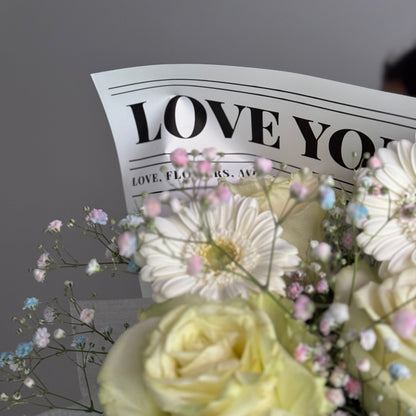 Bouquet of flowers with a piece of paper reading 'I love you' on a gray background