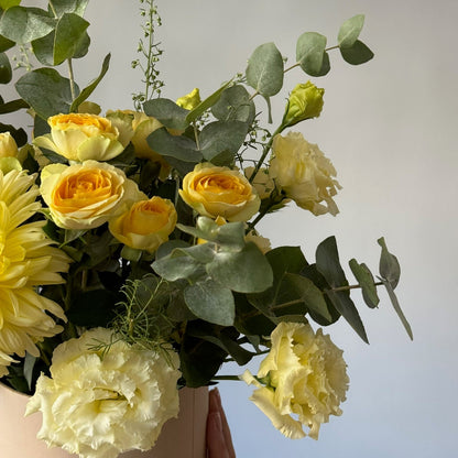 Bouquet of yellow flowers with greenery against a neutral background
