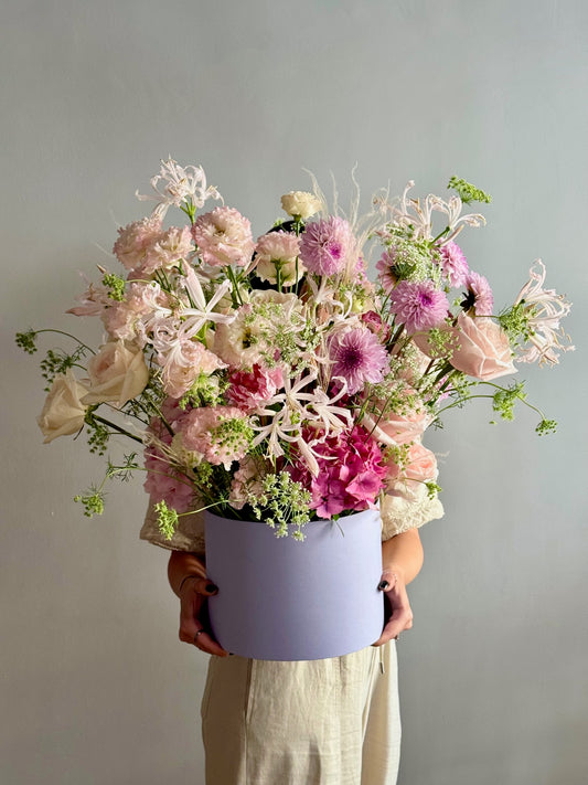 Person holding a bouquet of flowers in a light purple box against a plain background