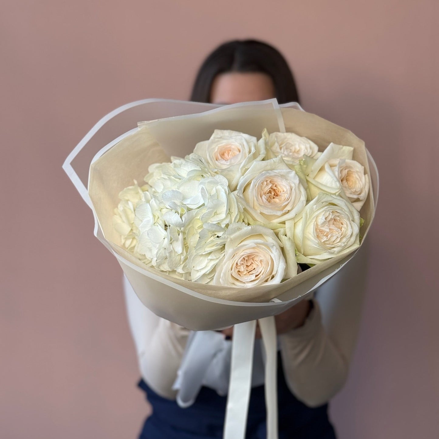 Bouquet of white and light pink roses held by a person against a plain background