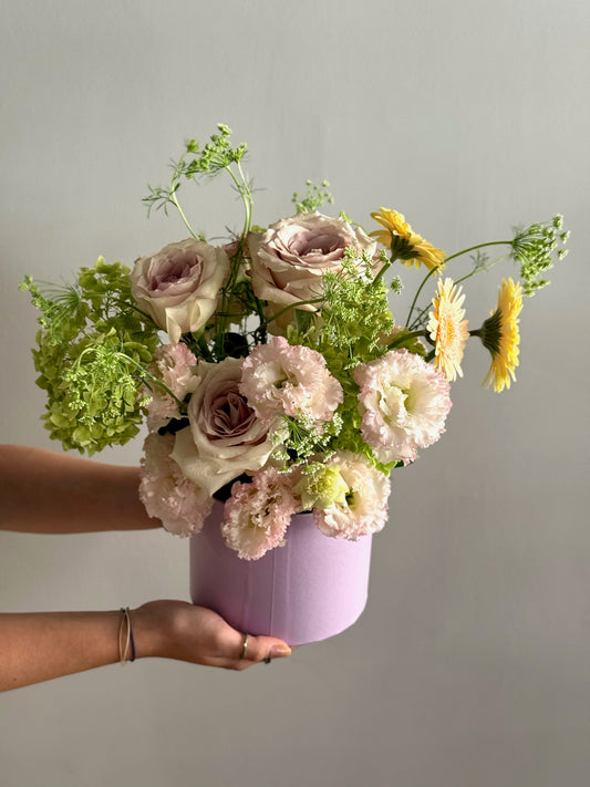 Person holding a bouquet of flowers in a purple box against a plain background