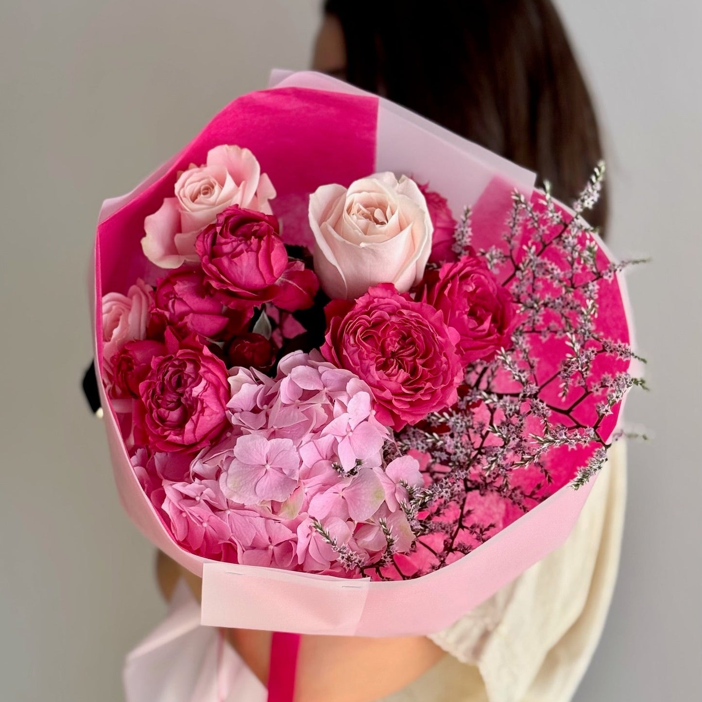 Bouquet of pink and red flowers wrapped in pink paper held by a person.