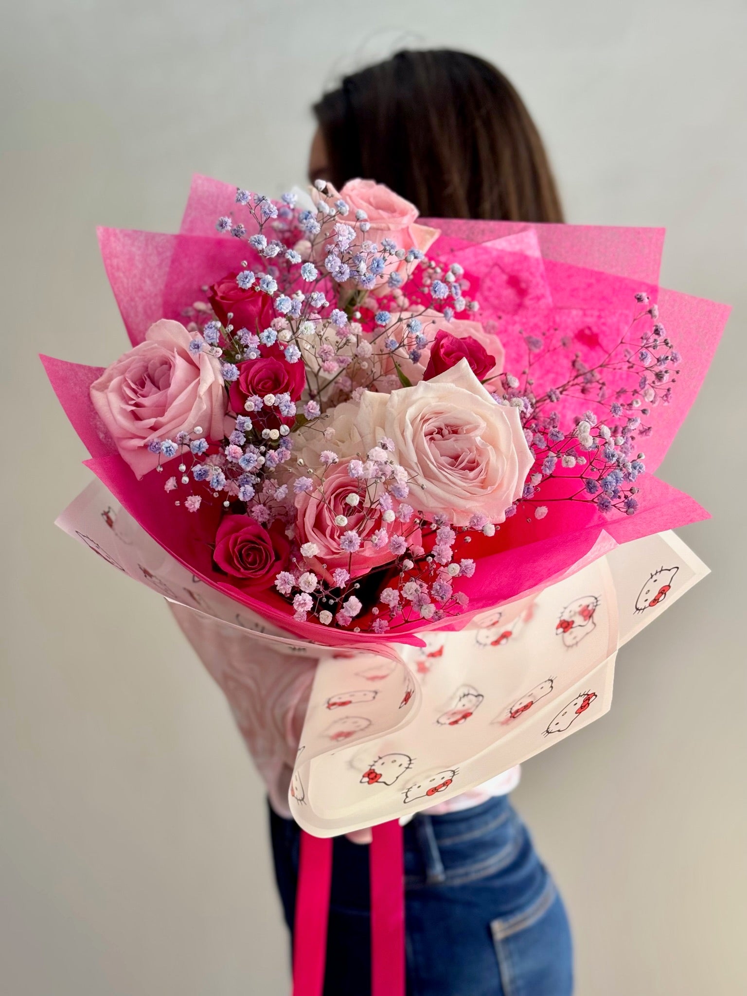 Person holding a bouquet of pink and white flowers wrapped in pink paper with a Hello Kitty design.