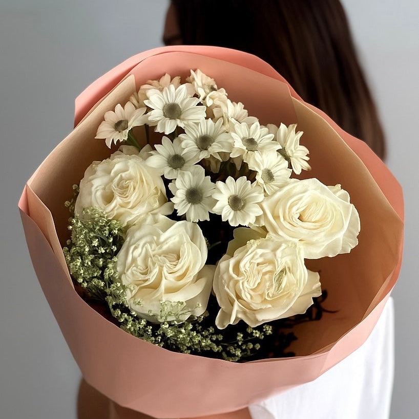 Bouquet of white flowers wrapped in brown paper held by a person against a neutral background
