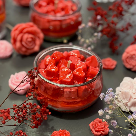 Red heart-shaped candles in glass jars with floral decorations on a dark surface