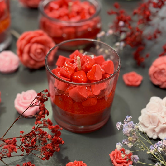 Glass container filled with red heart-shaped objects on a dark surface with decorative flowers.