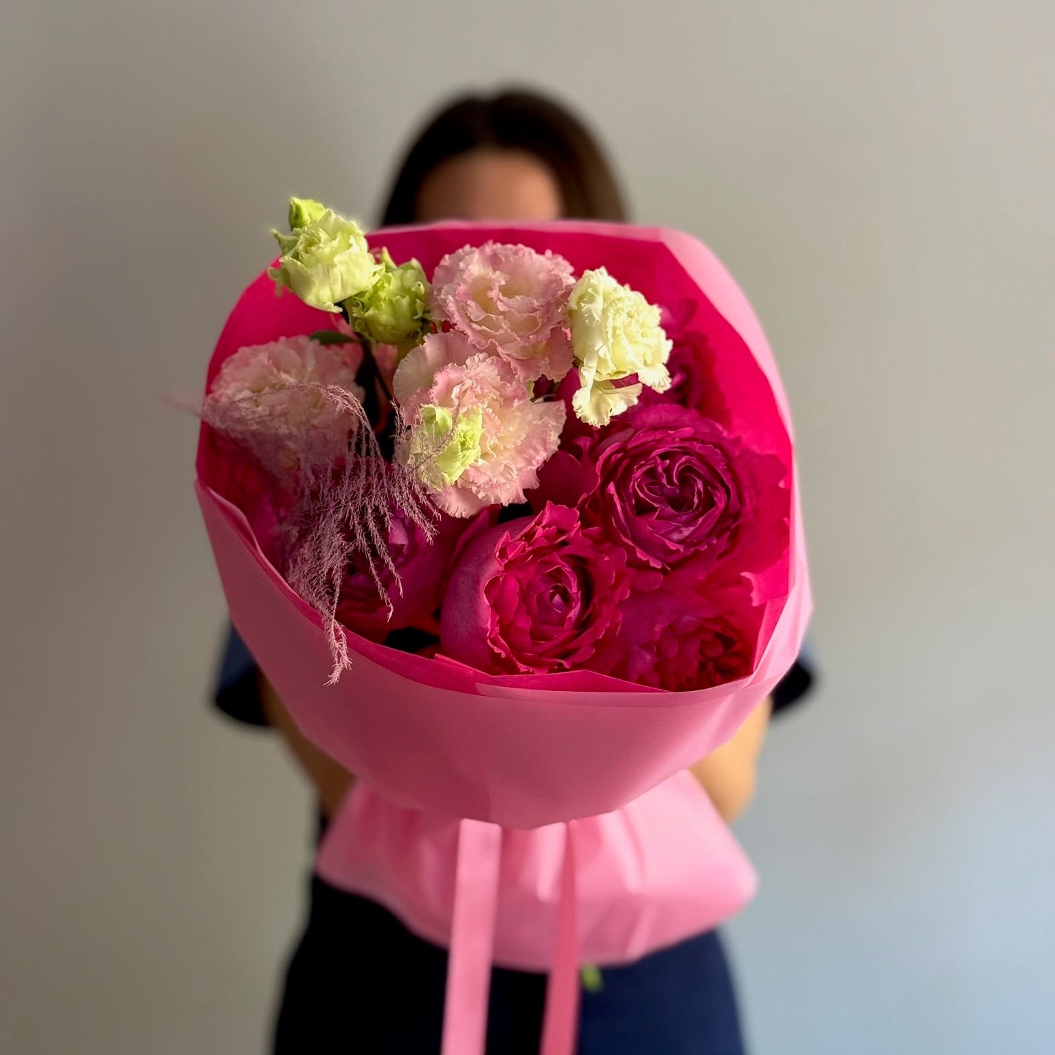 Person holding a bouquet of pink and green flowers wrapped in pink paper against a neutral background