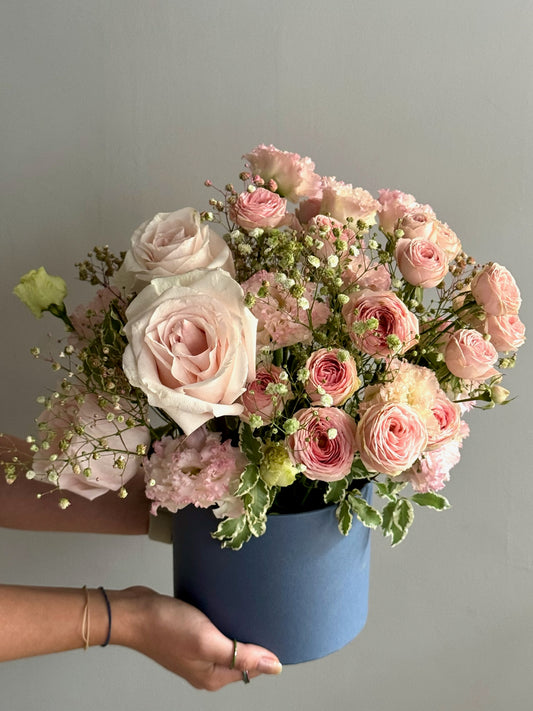 Bouquet of pink and white roses in a blue container held by a person against a gray background