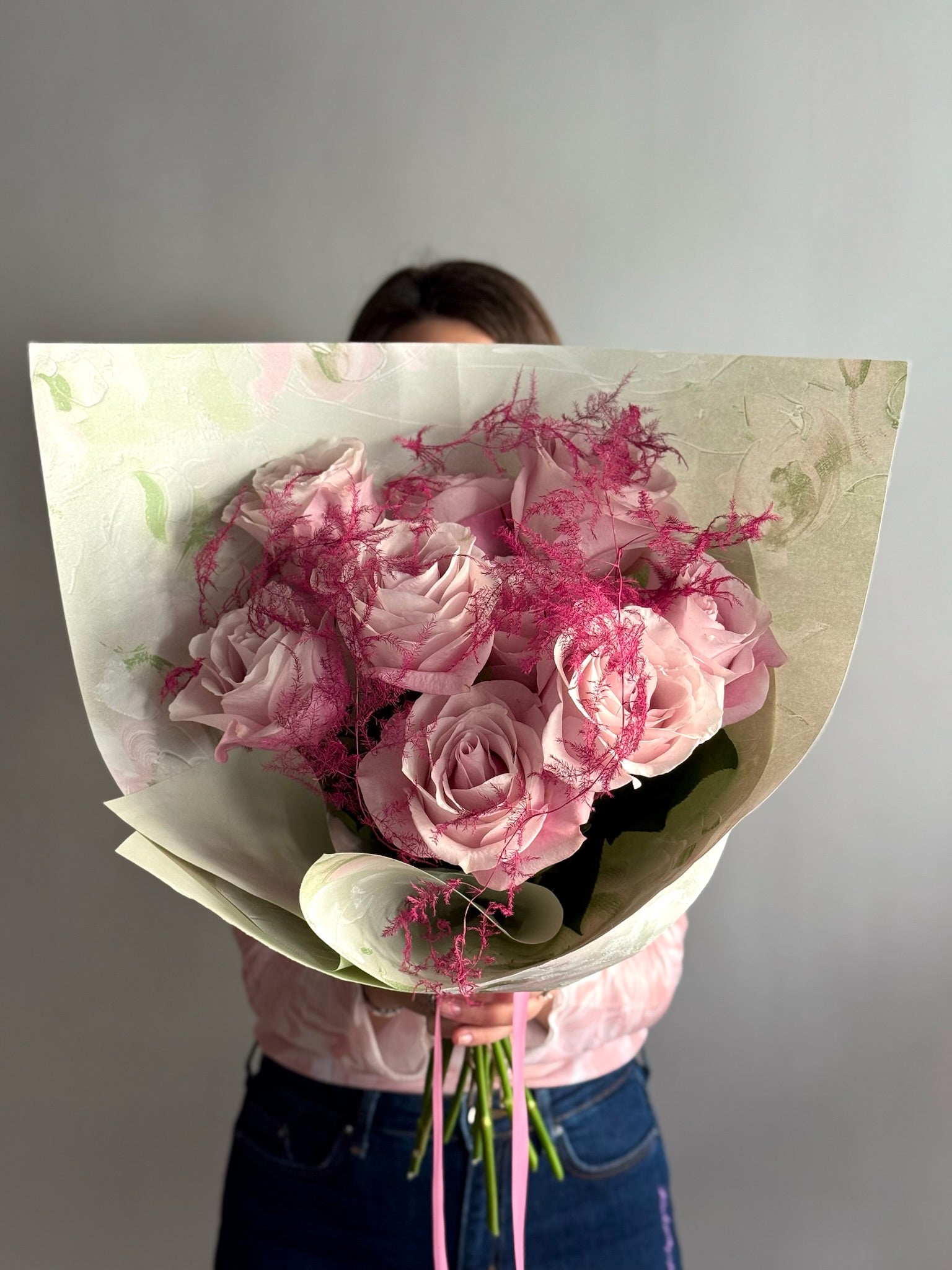 Bouquet of pink flowers wrapped in paper held by a person against a gray background