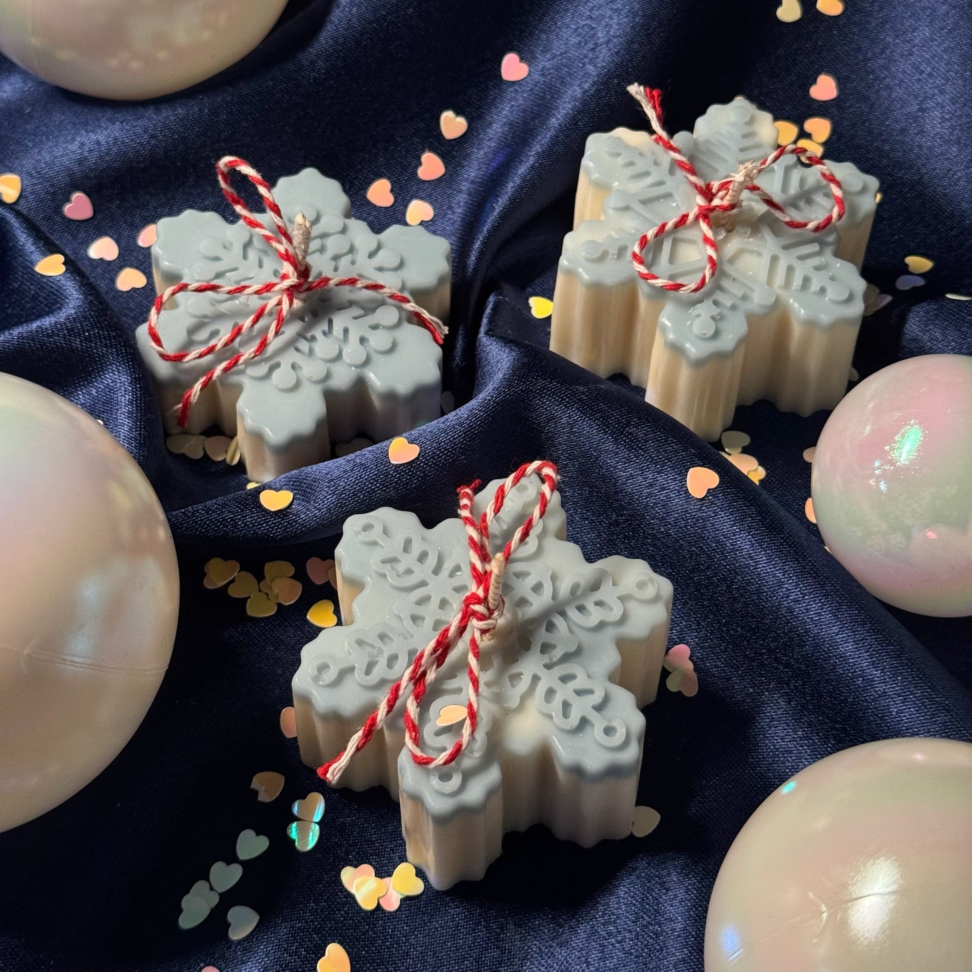 Snowflake-shaped soap bars with red string on a dark fabric background