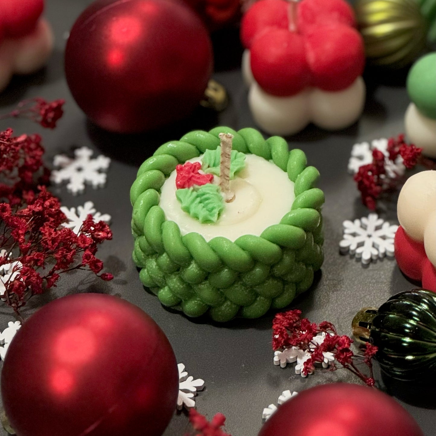 Decorative cake with green icing and a candle, surrounded by Christmas ornaments and flowers.