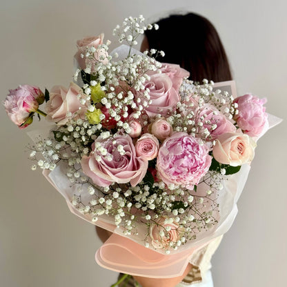 Bouquet of pink roses and baby's breath held by a person against a neutral background